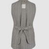 The long, fitted vest features a stand collar, a welt breast pocket, and pockets with pointed flaps.