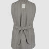 The long, fitted vest features a stand collar, a welt breast pocket, and pockets with pointed flaps.