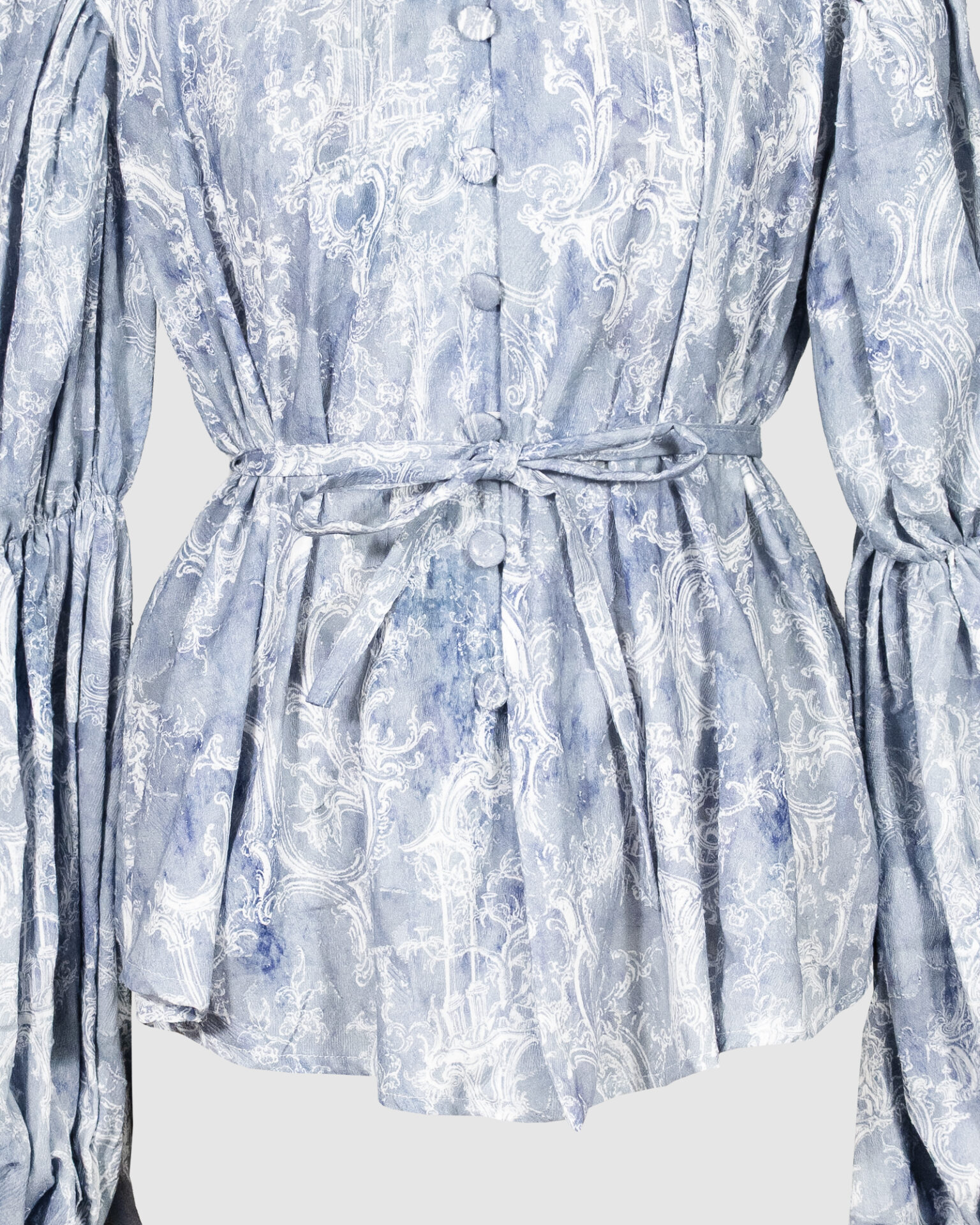 This loose-fitting blouse features a softly pointed front hem, a stand collar accented with a short ruffle, and a front button closure.