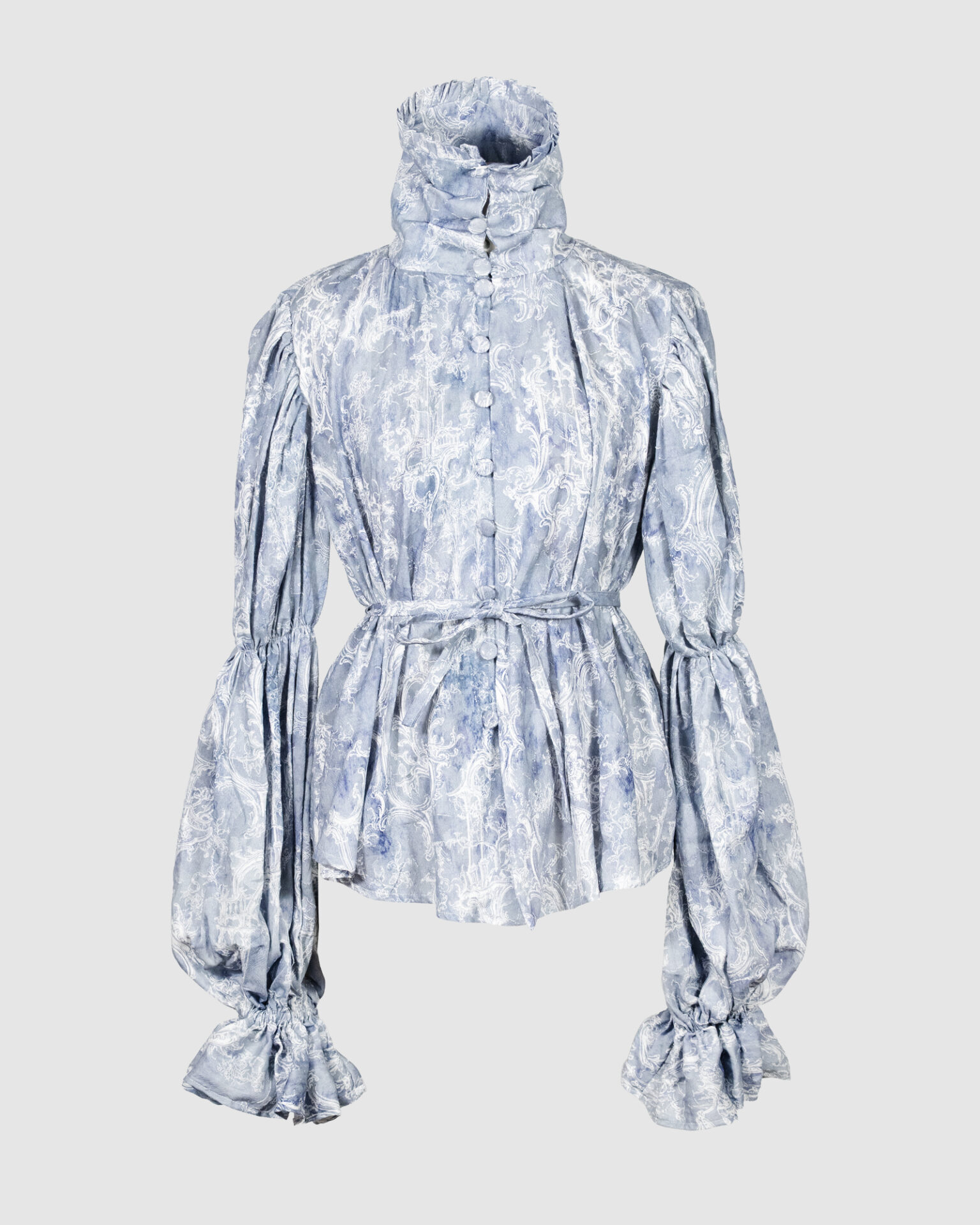 This loose-fitting blouse features a softly pointed front hem, a stand collar accented with a short ruffle, and a front button closure.