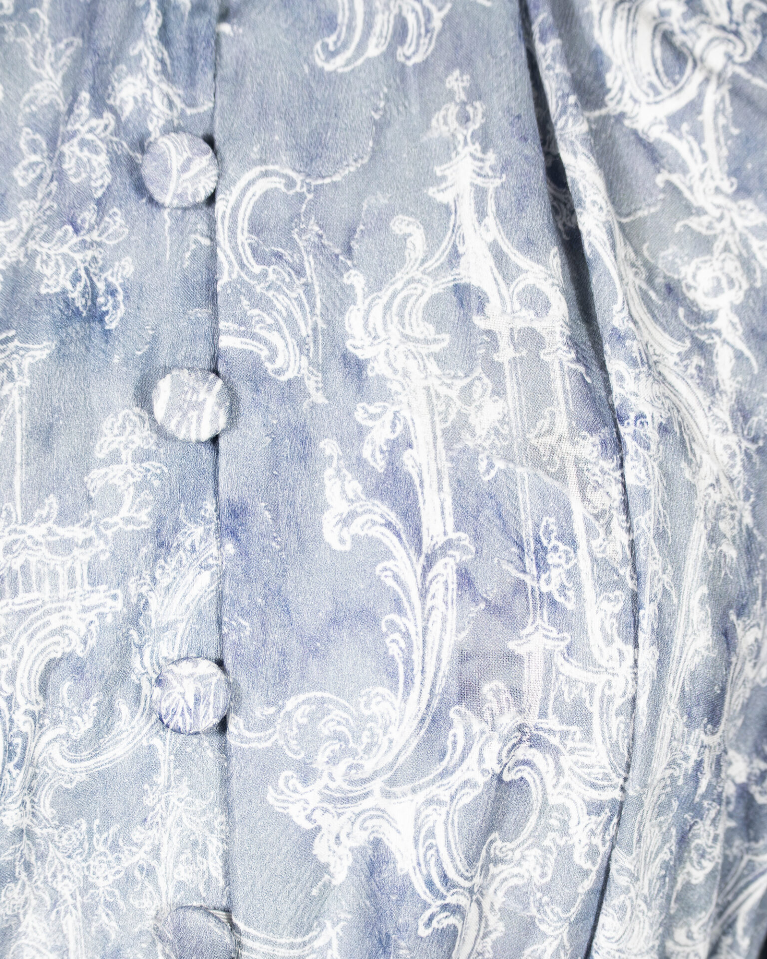 This loose-fitting blouse features a softly pointed front hem, a stand collar accented with a short ruffle, and a front button closure.