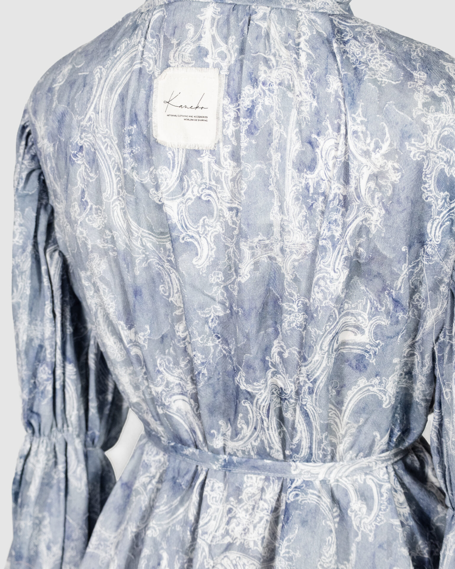 This loose-fitting blouse features a softly pointed front hem, a stand collar accented with a short ruffle, and a front button closure.