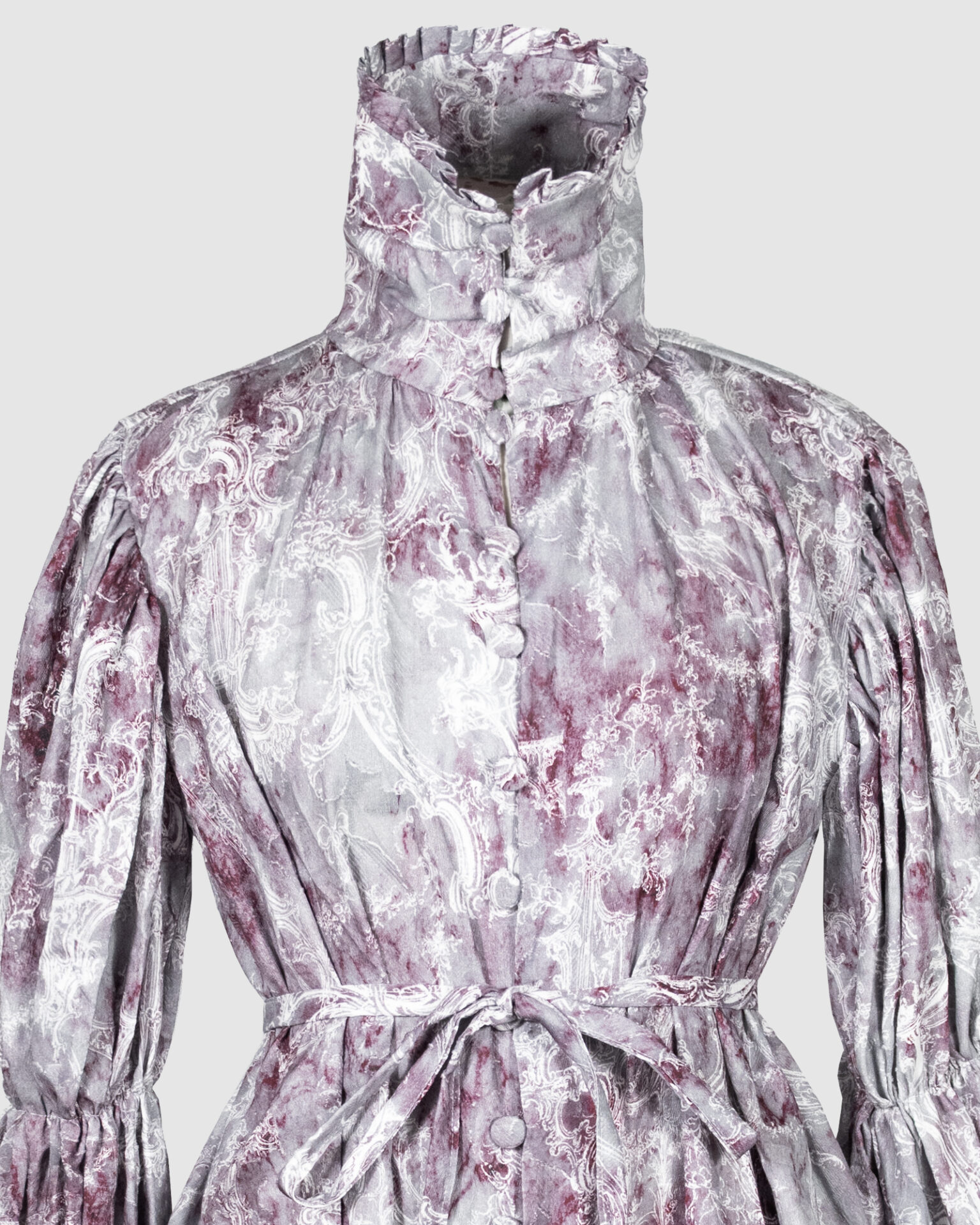 This loose-fitting blouse features a softly pointed front hem, a stand collar accented with a short ruffle, and a front button closure.