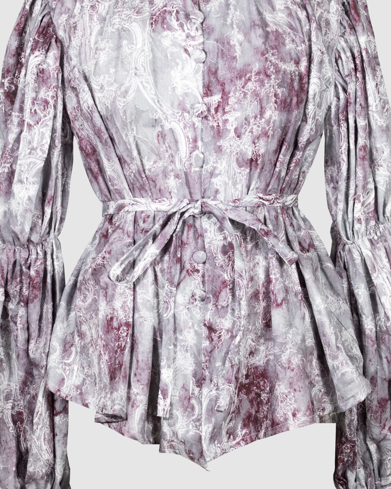 This loose-fitting blouse features a softly pointed front hem, a stand collar accented with a short ruffle, and a front button closure.