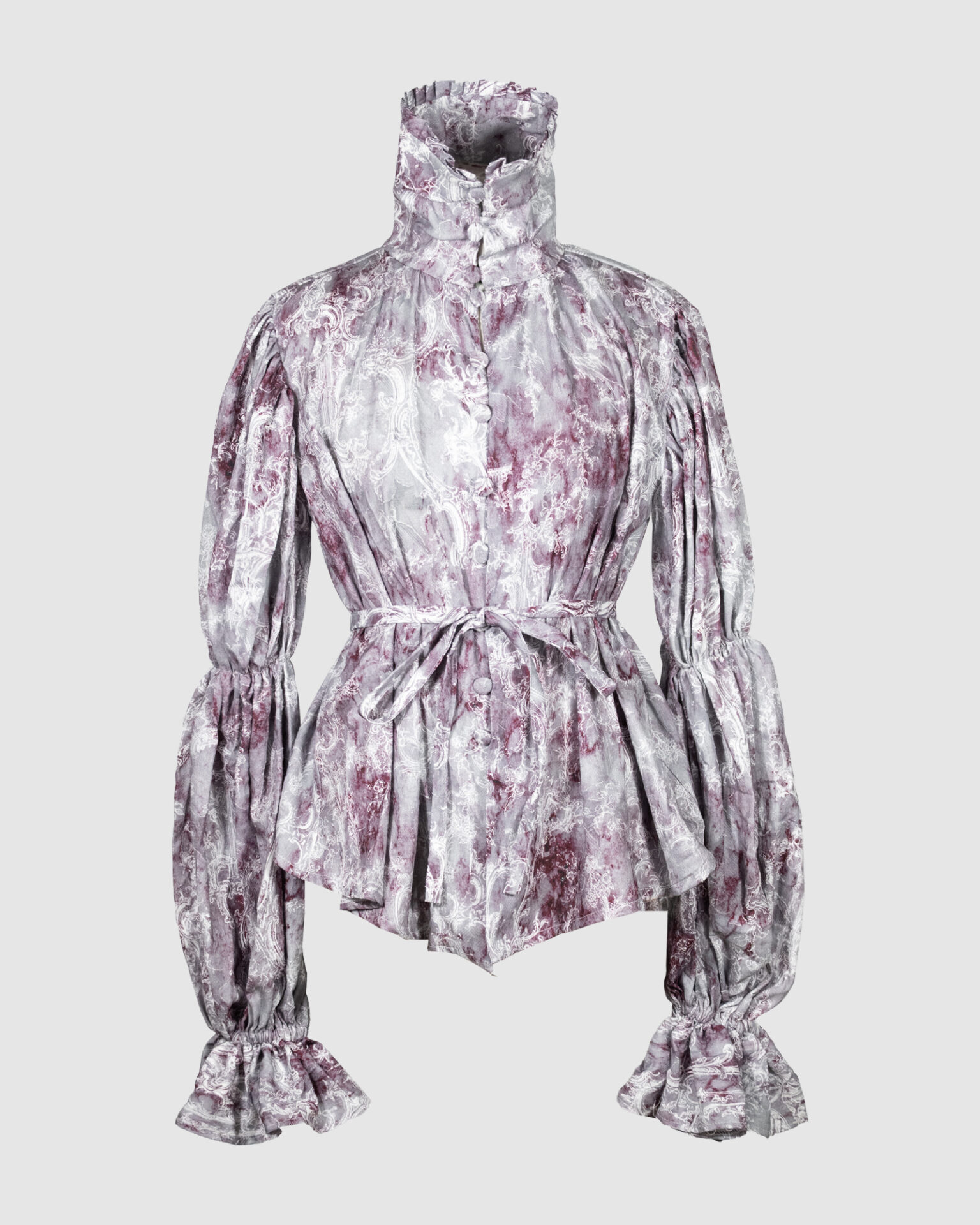 This loose-fitting blouse features a softly pointed front hem, a stand collar accented with a short ruffle, and a front button closure.