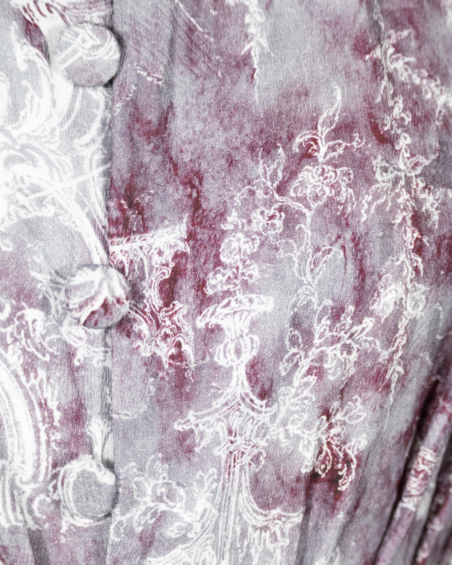 This loose-fitting blouse features a softly pointed front hem, a stand collar accented with a short ruffle, and a front button closure.