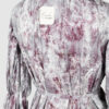 This loose-fitting blouse features a softly pointed front hem, a stand collar accented with a short ruffle, and a front button closure.