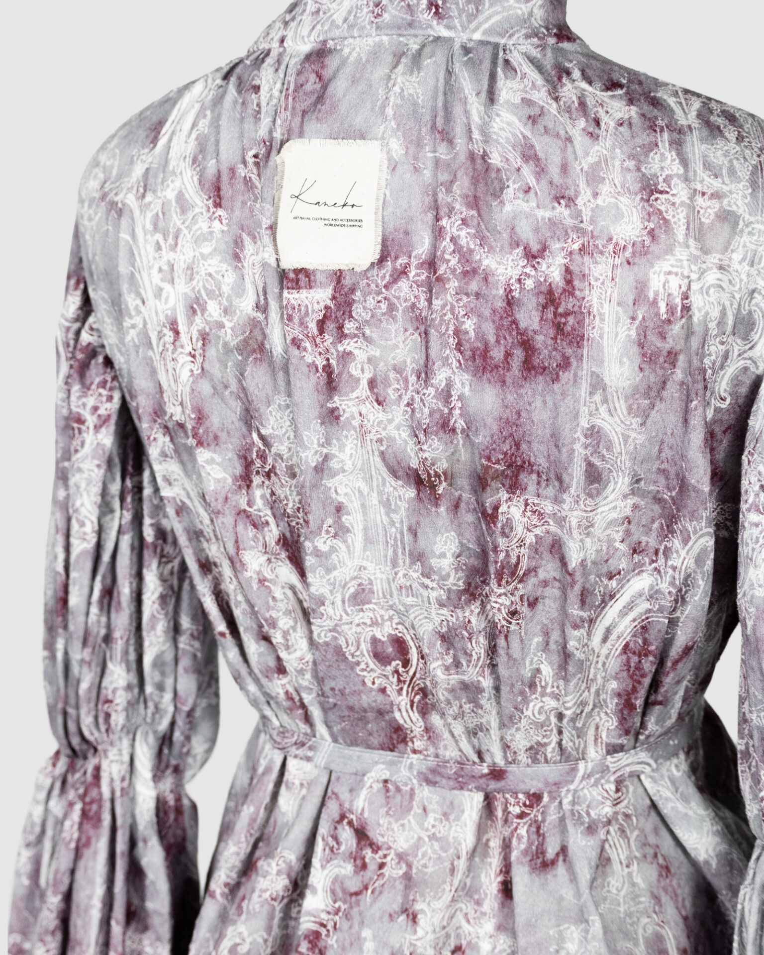 This loose-fitting blouse features a softly pointed front hem, a stand collar accented with a short ruffle, and a front button closure.
