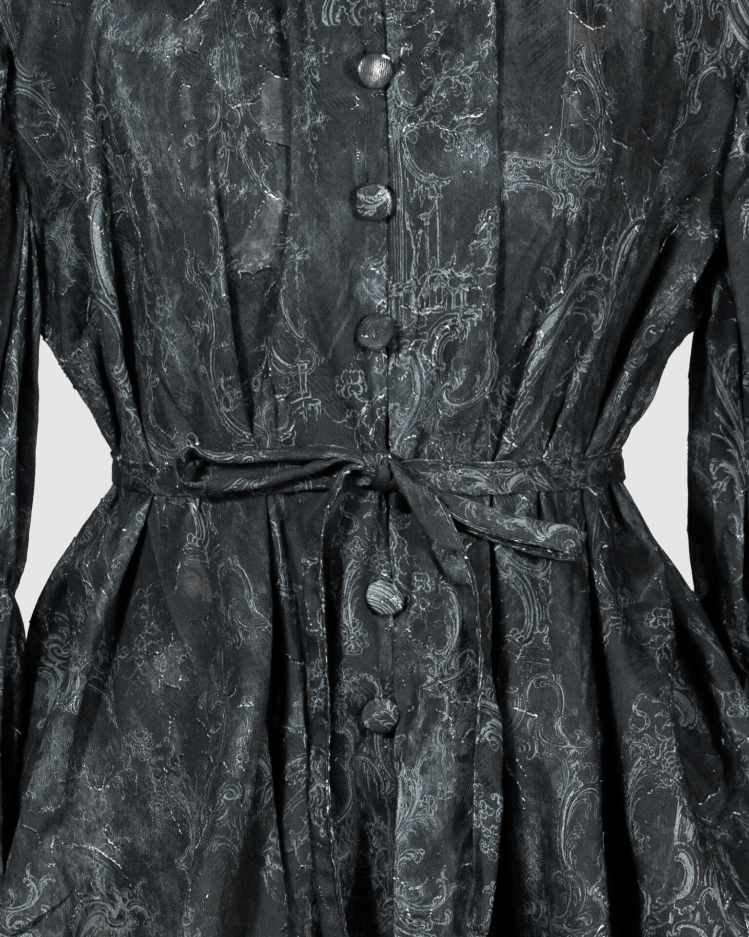 This loose-fitting blouse features a softly pointed front hem, a stand collar accented with a short ruffle, and a front button closure.