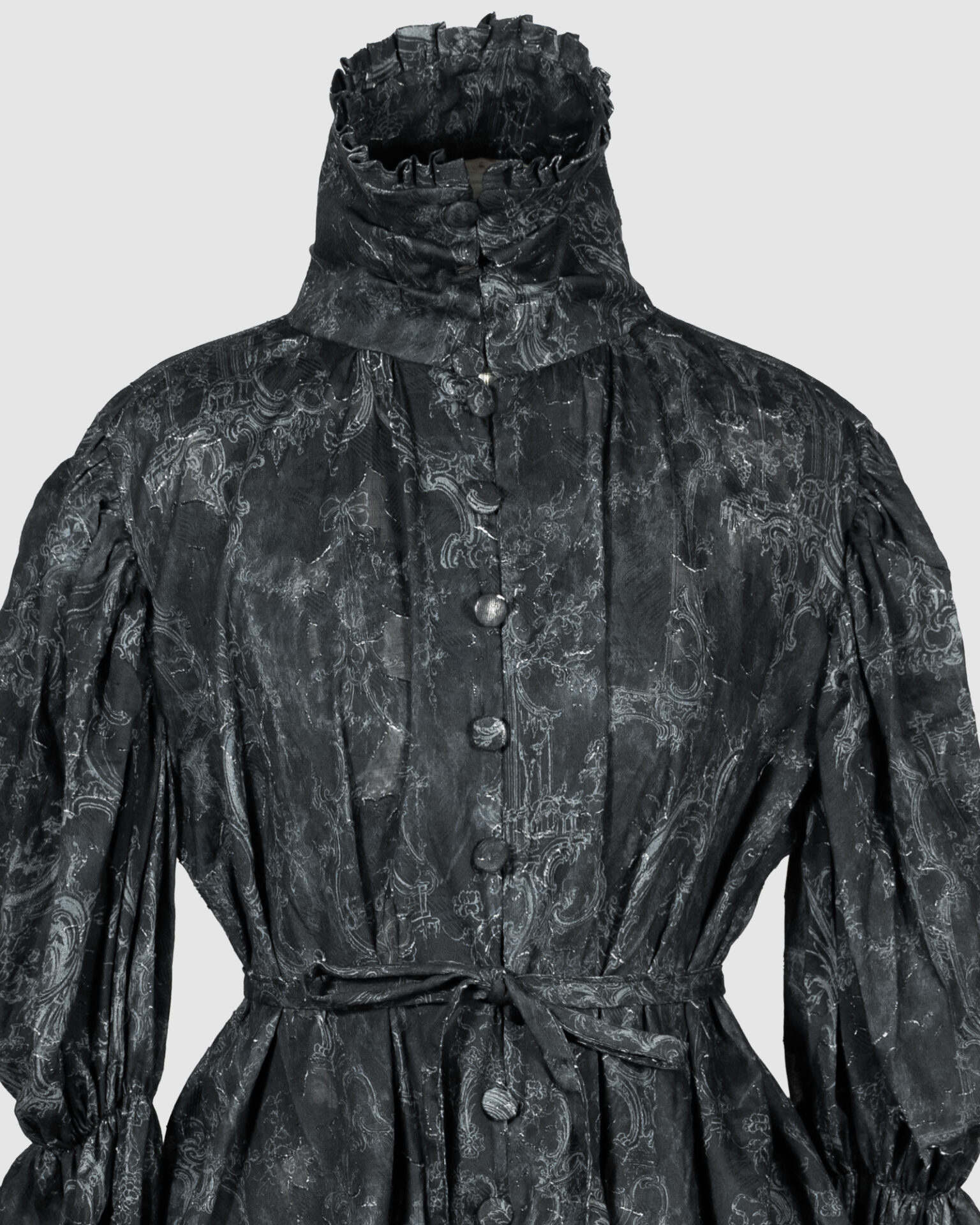 This loose-fitting blouse features a softly pointed front hem, a stand collar accented with a short ruffle, and a front button closure.