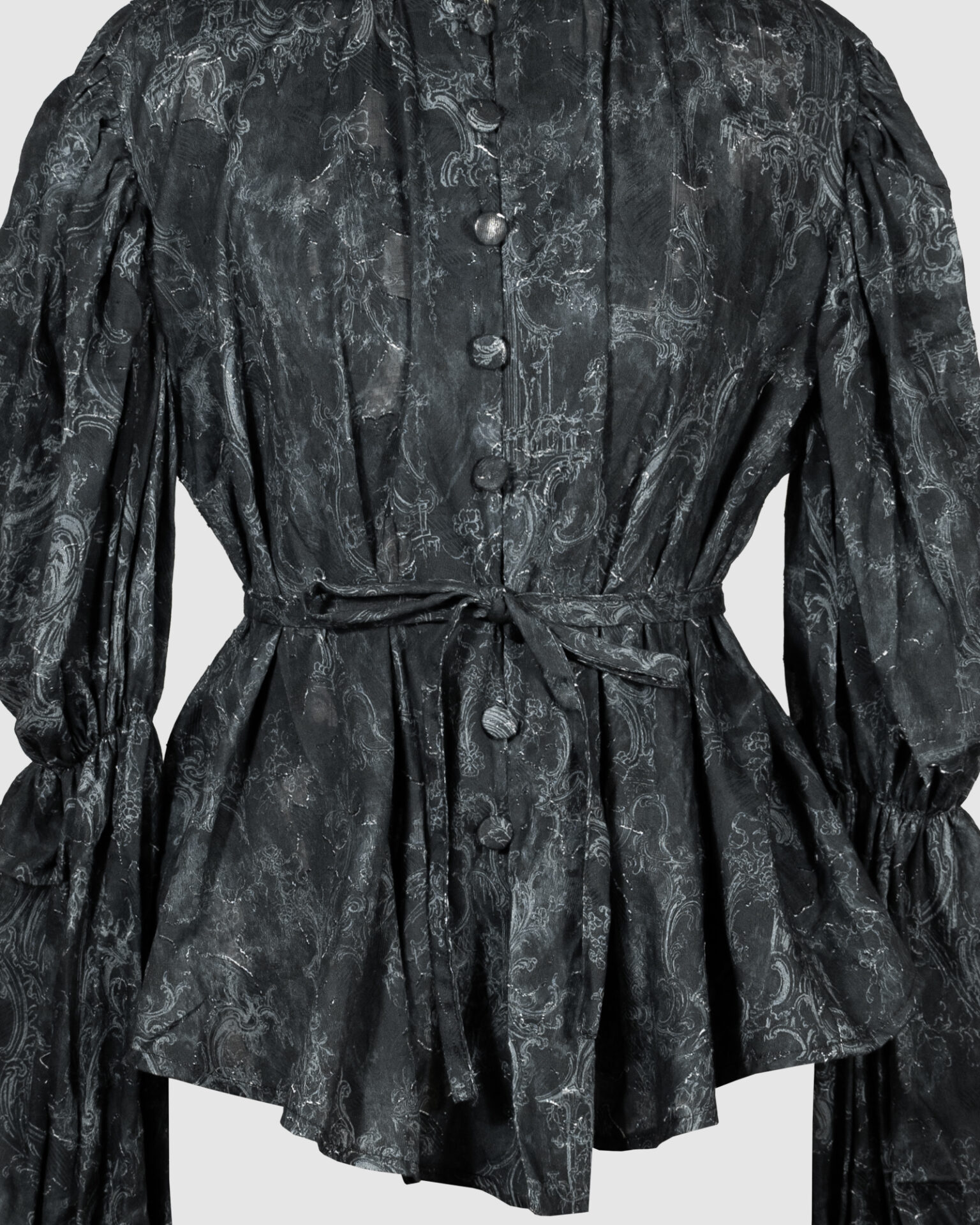This loose-fitting blouse features a softly pointed front hem, a stand collar accented with a short ruffle, and a front button closure.