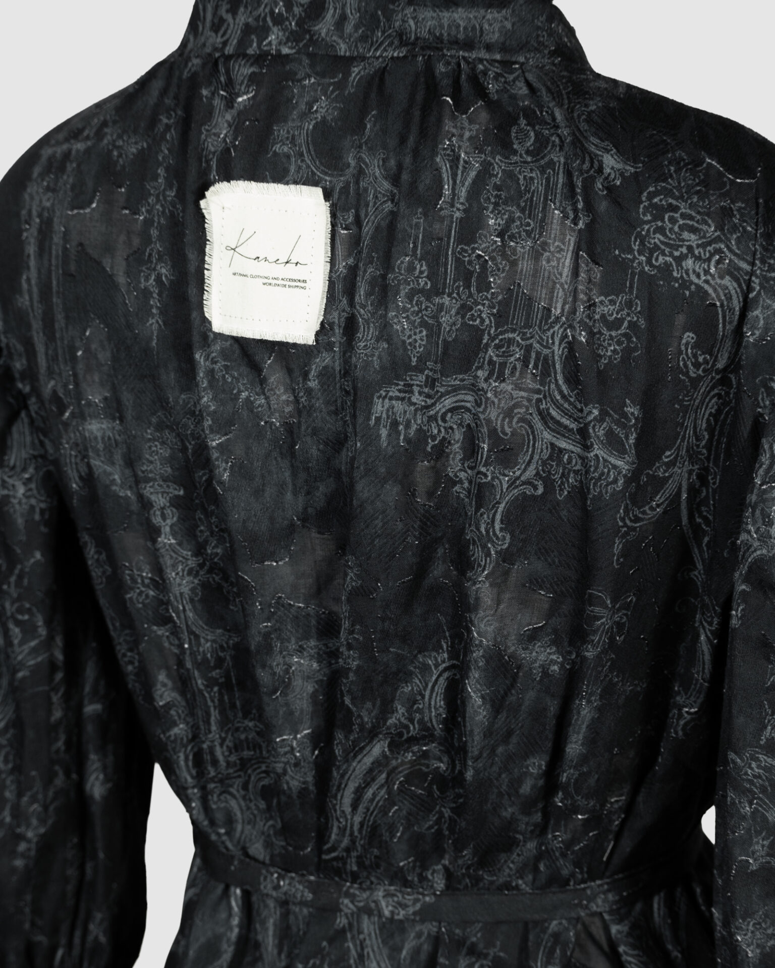 This loose-fitting blouse features a softly pointed front hem, a stand collar accented with a short ruffle, and a front button closure.